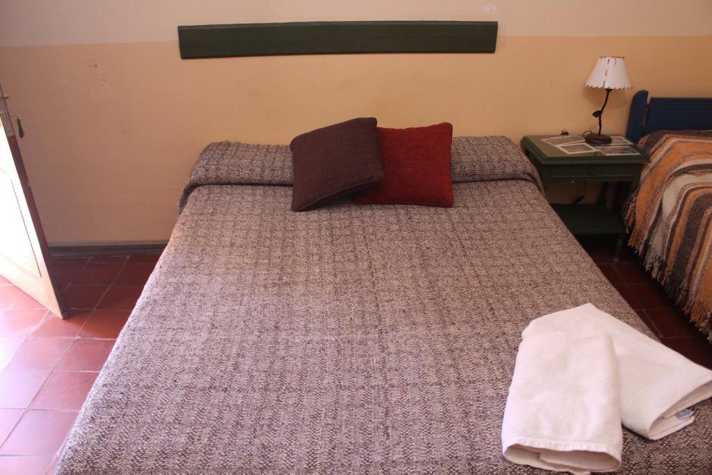 Cama matrimonial con almohadones y toallas en una habitación del hostal